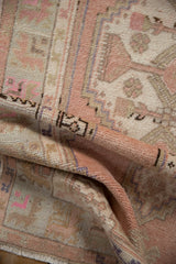 Folded distressed vintage Oushak runner showcasing its soft rose, sand pile and geometric pattern.