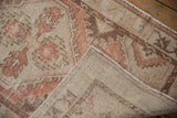 Distressed Oushak rug corner showcasing worn blush and beige pile, revealing hand-knotted foundation.
