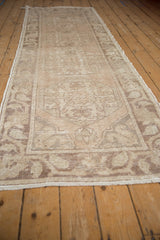 Distressed Oushak runner's short pile, featuring worn beige and ivory floral patterns.