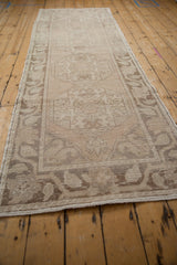 Distressed vintage Oushak runner's worn texture with subtle antique ivory and coffee brown floral designs.