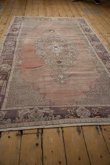 Decorative distressed Oushak rug featuring muted aubergine border and faded rose field.