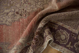 Folded distressed Oushak rug, revealing worn texture and muted rose patterns.