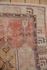 Distressed Turkish Oushak rug corner with ivory fringe, cantaloupe floral patterns, and wear.