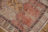 Distressed vintage Oushak rug corner: cantaloupe field, geometric aubergine border, and worn pile.