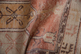 Vintage distressed Oushak rug showing folded cantaloupe, ivory, and aubergine floral motifs.