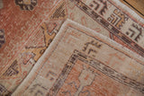 Distressed Oushak rug corner: cantaloupe, ivory, aubergine pile showing wear to knot heads.