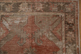 Distressed Oushak rug corner revealing foundation and faded floral patterns in madder red and brown.
