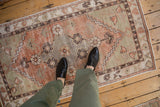 Terracotta and sage green floral medallion of a distressed Oushak runner with foundation showing.