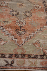 Distressed Oushak rug with worn terracotta and sage green pile, exposing foundation details.