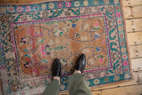 Distressed Oushak rug's worn pile, faded rust field, scrolling vinery, and colorful floral border.