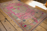 Fringed corner of a distressed Oushak rug, highlighting hot pink motifs and time-softened tones.