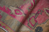 Distressed Oushak rug close-up: hot pink, dusty gold, and green-grey pile with subtle wear.