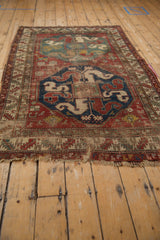 Close-up of antique Caucasian rug's stylized animals and floral motifs, showing wear and foundation.