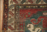 Geometric cherry red and mallard green border of antique Caucasian rug, with visible foundation wear.