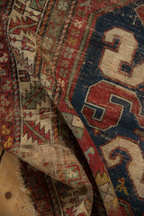 Detail of Antique Caucasian rug, cherry red and navy geometric patterns, exposed foundation, tattered ends.