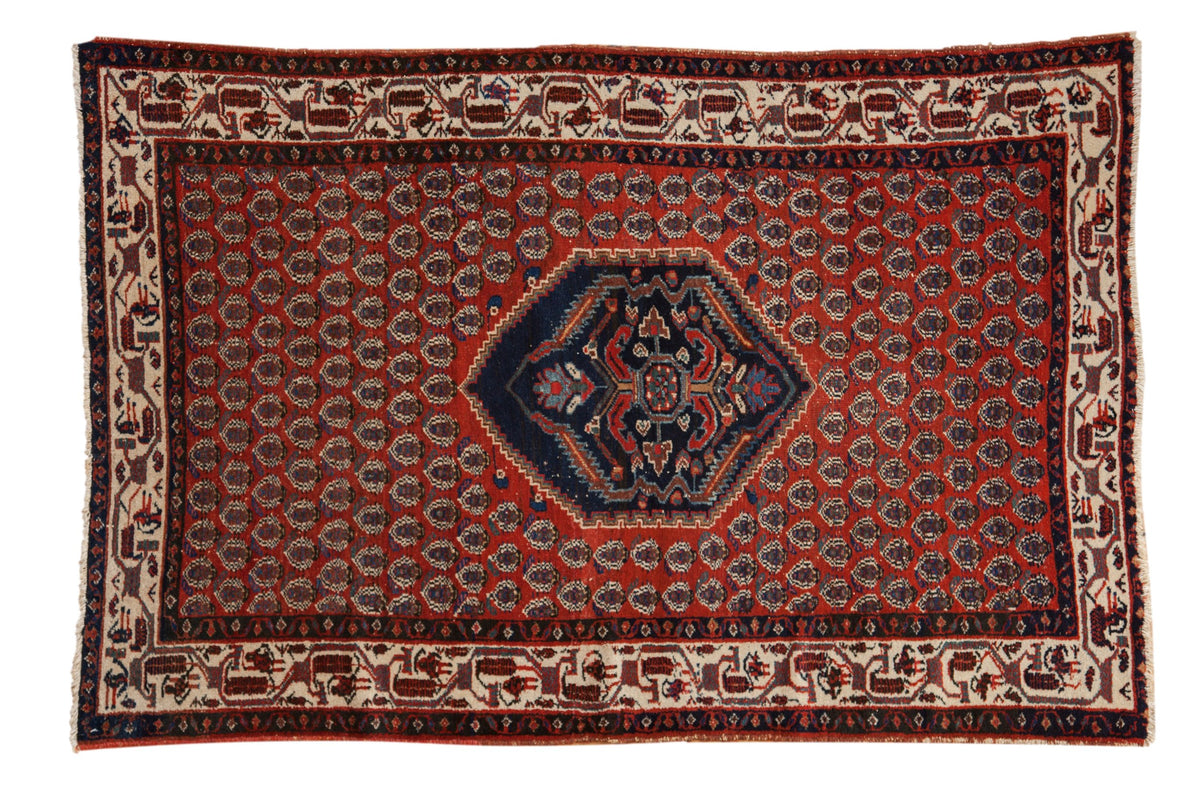 Vintage Serbend rug with a navy shield medallion on a brick red field of repeating staggered motifs.