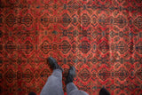 Distressed vintage Borchalou carpet close-up, showing worn floral medallions in red and navy.