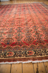 Distressed vintage Persian carpet corner: worn fringe, geometric border, raspberry field.