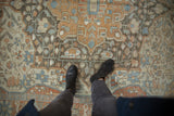 Distressed vintage Malayer carpet with floral pinwheel motifs in terracotta, blue, and ivory tones.