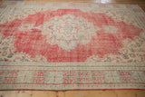 Distressed Oushak rug corner showing geometric border, floral spandrel, and worn faded cherry red.