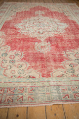 Distressed vintage Oushak carpet with worn cherry red, ivory, and turquoise patterns.