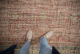 Distressed Oushak carpet pattern, worn red, ivory, green palmettes and vines, seen with shoes.