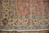 Distressed Oushak rug corner with worn pile, exposed foundation, ivory fringe, and faded blue-red border.