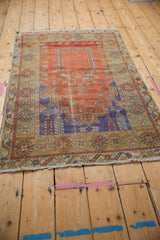 Distressed corner of a vintage Melas rug showing worn pile, colorful border motifs, and fringe.