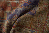 Distressed Melas rug detail, showing worn royal purple, terracotta, and abstract plant motifs.