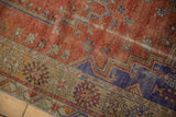 Distressed vintage Melas rug corner displaying brick red, royal blue, and pale yellow geometric designs.