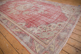 Distressed Oushak carpet corner, showing faded cherry red, ivory, and mauve floral vinery.