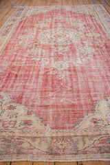 Distressed Oushak carpet pile showing worn cherry red and ivory, with faded floral pattern.