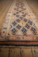 Distressed vintage Kurd runner with geometric navy motifs on tangerine and beige diamond panels, showing varied pile.