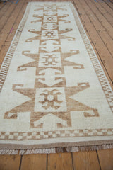 Angled view of repeating brown geometric medallions on a cream vintage Kurd runner.