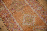 Distressed pile texture of a vintage Kurd runner, showing faded orange and pale fuchsia geometric motifs.