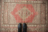 Distressed vintage Kula rug with visible wear, featuring a faded cherry red medallion on a beige field.