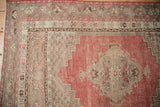 Distressed Kula rug corner: dusty red field with wear, stylized beige borders, and red selvage.