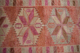 Close view of distressed hand-knotted pile showing pinwheel designs in pink, fuchsia, and dusty red.