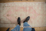 Feet on distressed Oushak runner, pink and ivory geometric stepped pattern, worn pile.