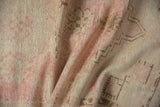 Distressed Oushak rug texture showing faded pink, ivory, and coffee bronze geometric motifs.