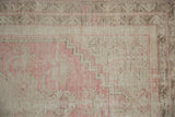 Distressed Oushak rug with faded pink and ivory stepped geometric motifs.