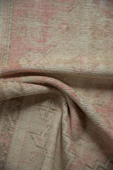 Distressed Oushak rug texture: soft pink and ivory tones with time-softened wear.