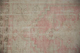 Distressed Oushak rug pile showing faded pink and ivory geometric motifs with visible foundation.