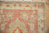 Distressed Oushak corner detail: pale raspberry blossoms, ivory border, and fine fringed edge.
