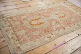 Distressed Oushak rug corner, showing fringe and mostly even wear on pale raspberry, ivory motifs.