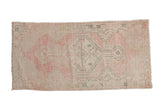 Vintage distressed Oushak runner with a geometric medallion in soft pink, ivory, and dusty green.