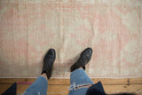 Distressed pink and beige Oushak rug runner's worn pile texture with boots on top.