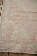 Distressed Oushak rug runner with faded traditional pink pattern on worn beige pile.
