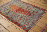 Distressed Oushak rug corner, faded cherry red border with floral motifs, evident wear.