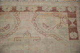 Distressed Oushak rug border with hour glass floral motifs in ivory, seafoam, and chestnut, showing wear.